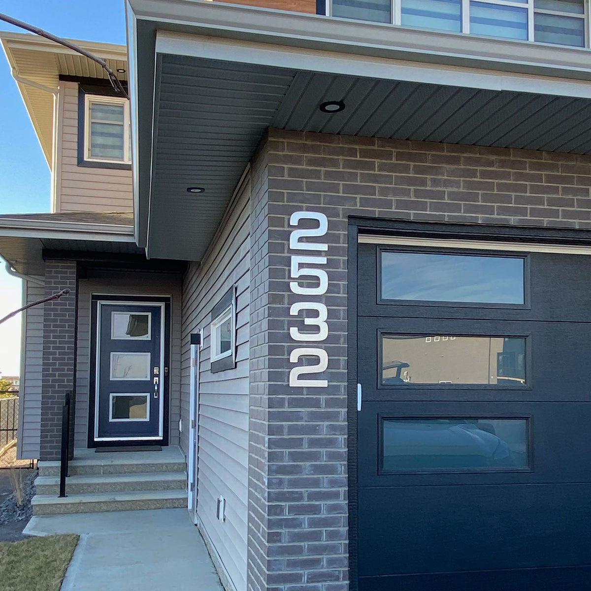 Vertical aluminum house numbers installed on brown brick wall